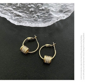 Detail of gold hoop earrings with cylinder zircon pendants on a black stone surface