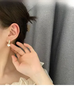 Close-up of a model wearing elegant heart-shaped pearl earrings with golden accents
