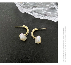 Macro detail of golden C-shaped heart earrings with zircon stones and pearlescent beads