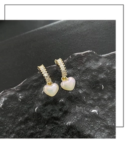 Detail of gold heart earrings with baguette-cut cubic zirconia and pearly white finish