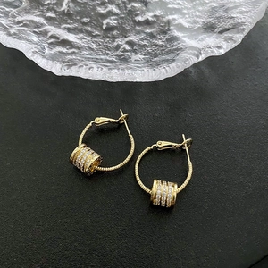 Fashionable 18K gold hoop earrings with zircon studded cylinder charm on dark surface