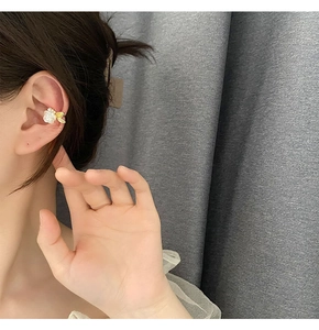 Détail de clip d'oreille rose blanche avec feuilles dorées et petites perles sur modèle