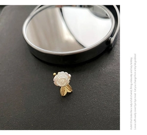 Gros plan sur une boucle d'oreille rose blanche irisée élégante avec feuilles dorées