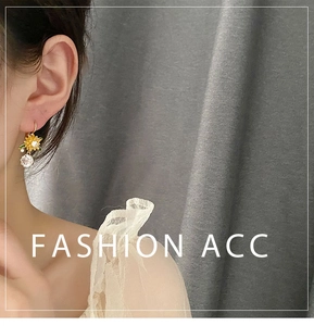 Detail of sunflower earring with yellow enamel and zircon hanging on model's ear