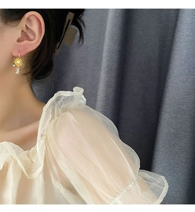 Detailed shot of sunflower earrings with yellow petals and drop pearl on a female model