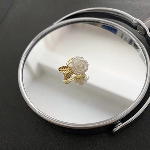 Bague vintage rose blanche à feuilles dorées sur fond de miroir avec reflets élégants
