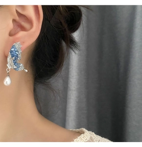 Detail of blue crystal butterfly wing earrings with a hanging white pearl drop