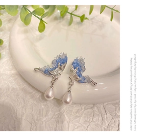 Macro shot of silver butterfly wing earrings with blue crystals and drop pearls