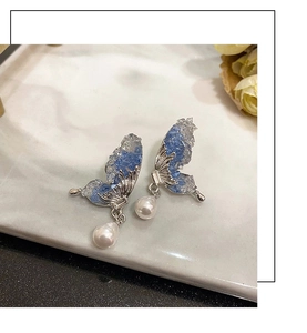 Detail of butterfly earrings with blue crushed stones and hanging white pearls