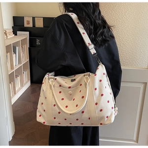 Detail of strawberry embroidery on a corduroy travel bag with an adjustable strap