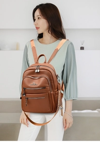 Detailed view of brown leather backpack with multiple zippers and geometric side straps