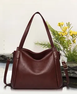 Detailed view of burgundy pebbled leather tote bag with gold hardware and strap on stone