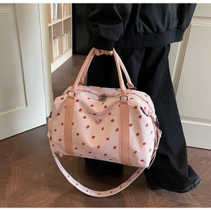 Detail of pink corduroy travel bag featuring red strawberry patterns and leather handles