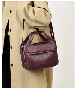 Detailed close-up of burgundy leather crossbody bag with pebble texture on beige coat