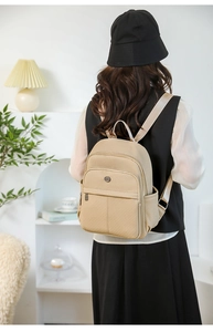 Detail of beige textile backpack showing front zipper pocket and side water bottle holder