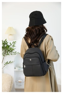 Detail of a black nylon backpack with multi-pocket design and metal logo on model