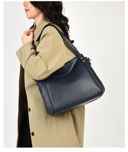 Navy blue leather tote bag with lychee texture and gold rivets on beige trench coat