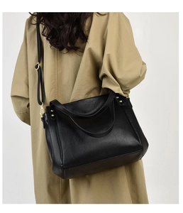 Side view of black pebble leather bucket bag with gold hardware on trench coat