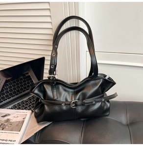 Détail du sac à bandoulière noir mat avec sangles à œillets métalliques sur un banc en cuir