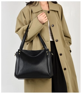 Detail of black pebbled leather tote bag with gold stud accents and long shoulder strap