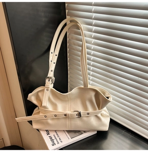 Détail du sac à bandoulière plissé blanc crème avec boucle en métal sur un livre blanc