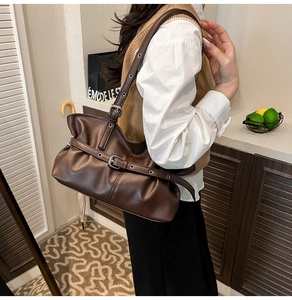 Détail d'un sac d'épaule marron foncé avec œillets argentés et plis porté par un mannequin