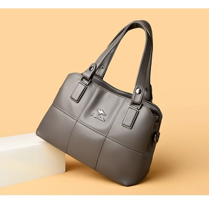 Gros plan sur la texture du cuir grainé et le logo métallique d'un sac à main gris