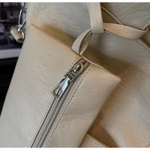 Close-up of smooth silver metal zipper on cream pebbled leather tote bag detail