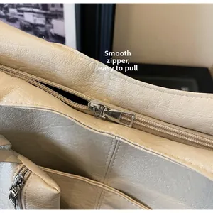 Detail of a smooth silver zipper on a beige pebble grain leather tote bag with soft texture