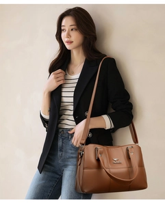 Détail d'un sac à main en cuir marron grainé avec logo métallique et coutures croisées