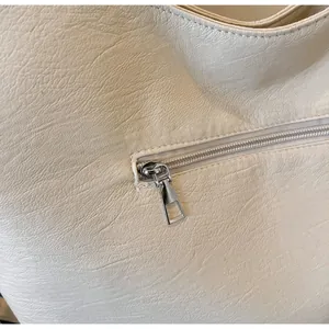 Detailed macro view of a smooth silver metal zipper on cream-colored soft PU leather tote