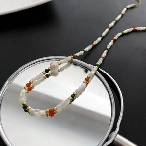 Beaded necklace with red, green, and gold beads featuring a large white baroque pearl