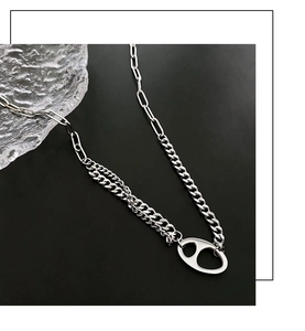 Gros plan d'un collier argenté avec chaîne asymétrique et pendentif géométrique moderne