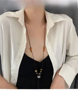 Detail of a woven cord necklace with amber beads and a vintage silver butterfly pendant