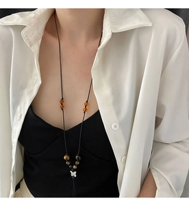 Close-up of a silver butterfly pendant on a braided rope necklace with amber beads
