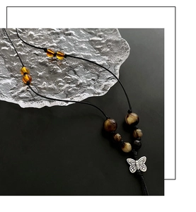 Detail of silver butterfly pendant with textured wings and amber beads on woven cord