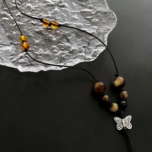 Bohemian black woven necklace with butterfly pendant and marble beads on glass background