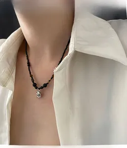 Detailaufnahme der schwarzen Perlenkette mit silbernem Blumenanhänger an einem Model in Weiß