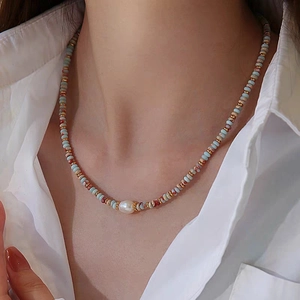 Detail of beaded necklace with light blue stones, red beads, and a baroque freshwater pearl