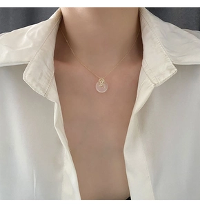 Détail d'un collier doré avec pendentif rond en jade porté sur une chemise blanche