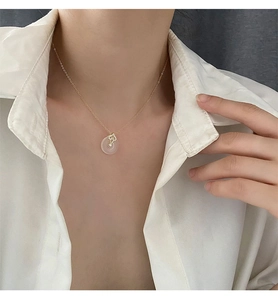 Gros plan d'un collier doré avec pendentif blanc sur une femme en chemise blanche