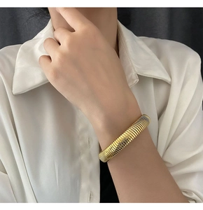 Detailed view of wide gold ribbed elastic bangle on wrist with white shirt