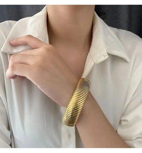 Detail of a wide gold ribbed cuff bracelet showing intricate metal texture on a model wrist