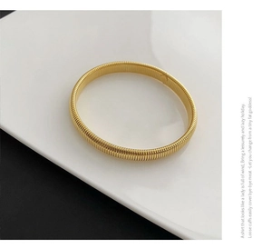 Detailed macro view of a golden threaded stretch bangle on a luxury ceramic display