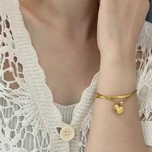 Close-up of double-layered gold heart pendant bracelet worn over cream crochet clothing