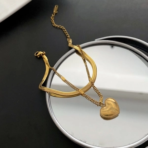 Detail of double-layer golden snake chain and thin link bracelet with heart pendant