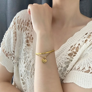 Detail of a double-layered gold heart pendant bracelet worn over a white lace sleeve