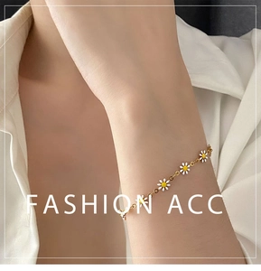 Close-up of a delicate golden chain bracelet with white and yellow enamel daisies