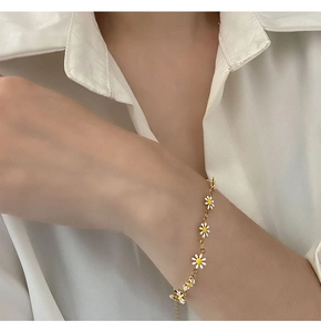 Detail view of a gold chain bracelet with white daisy charms worn on a white shirt