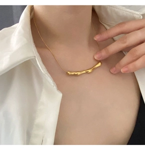 Dettaglio della collana con pendente ondulato in oro indossata da una modella